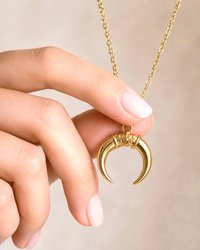 Close up of gold crescent pendant necklace held by hand with elegant cable chain jewelry styling