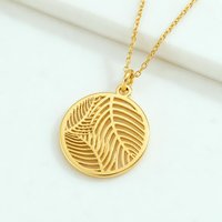 Gold palm leaf pendant necklace hanging on white background with soft lighting