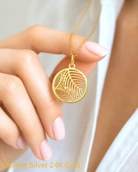 Close up hand holding gold palm leaf charm pendant necklace