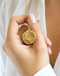 Close up hand holding gold palm leaf charm pendant necklace
