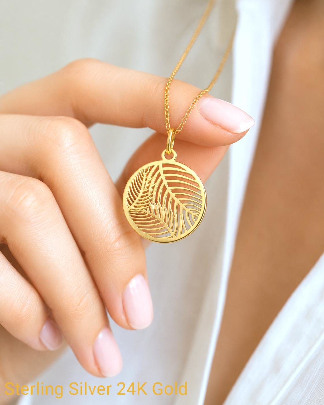 Close up hand holding gold palm leaf charm pendant necklace