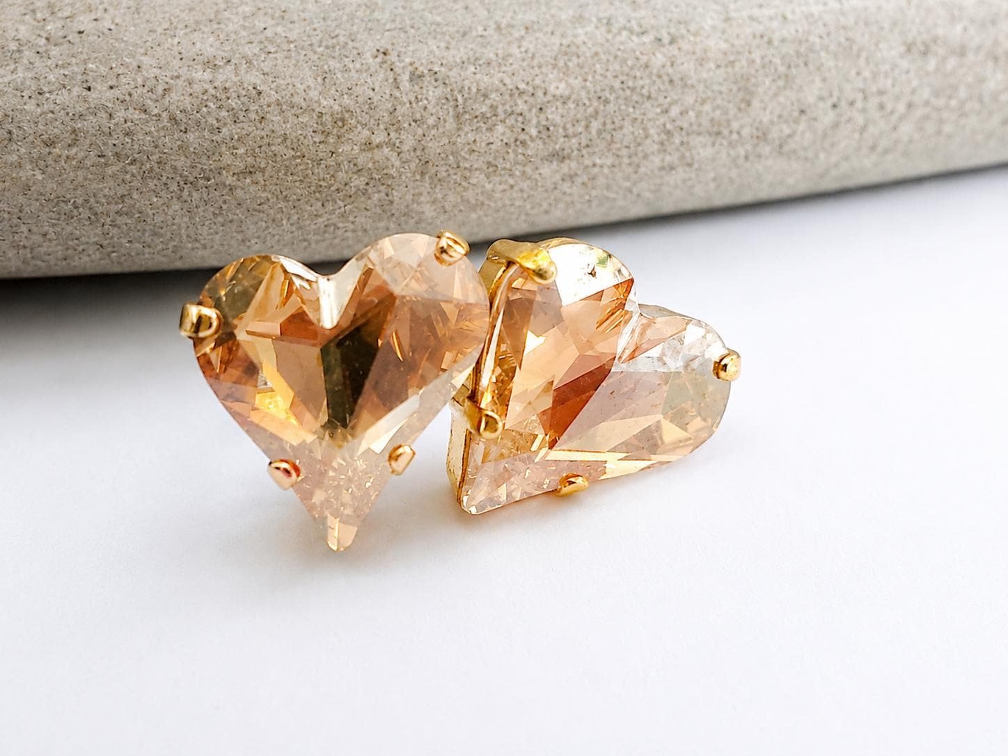 Close-up of champagne heart crystal stud earrings made with Swarovski Crystals, set in gold plated prong settings with brilliant faceted sparkle.