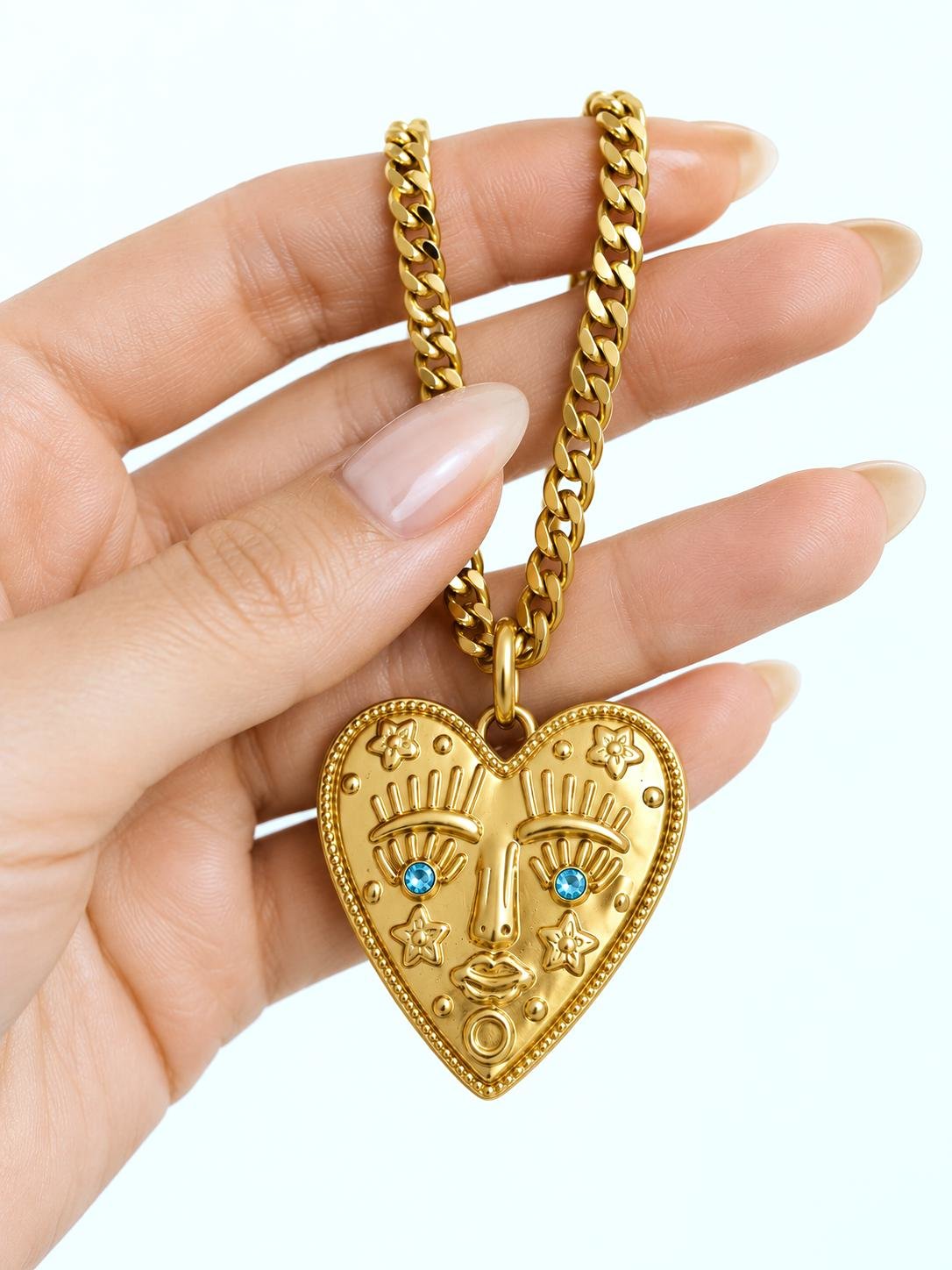 Chunky gold stainless steel heart face necklace with aquamarine crystal eyes on a thick curb chain.