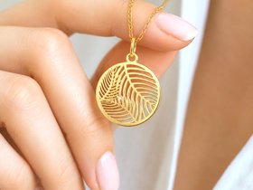 Close up hand holding gold palm leaf charm pendant necklace